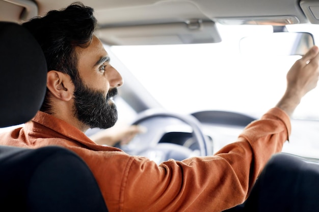 Vue arrière d'un homme indien conduisant une voiture et réglant le miroir