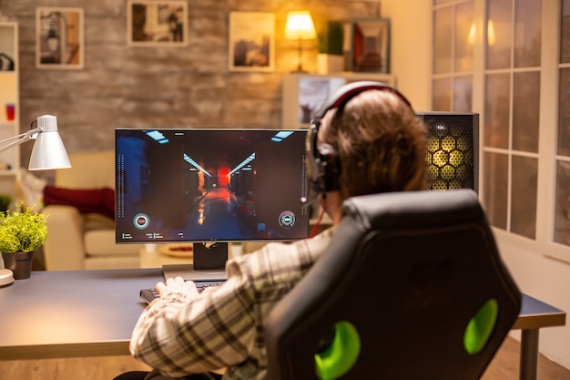 Vue arrière d'un homme joueur jouant à un jeu de tir sur son puissant ordinateur PC tard dans la nuit dans le salon.
