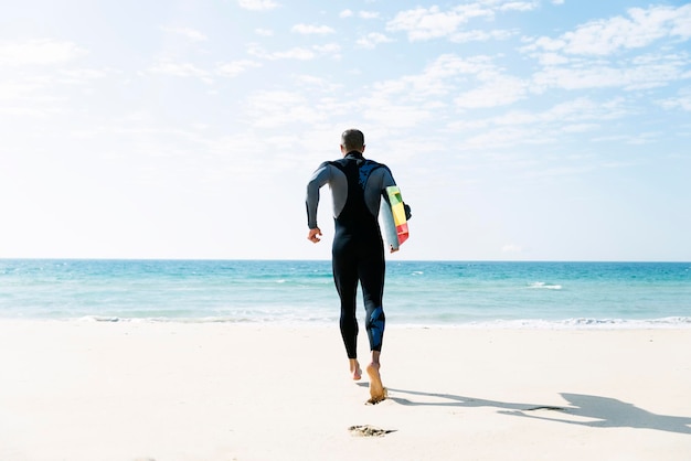 Vue arrière d'un homme avec un kiteboard qui court sur la plage
