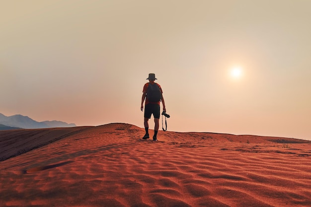 Photo vue arrière d'un homme marchant dans le désert contre le ciel au coucher du soleil