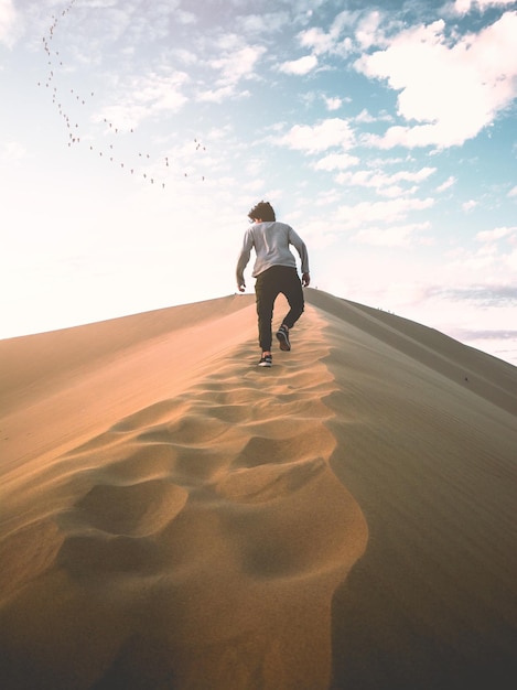 Vue arrière d'un homme marchant sur le sable contre le ciel