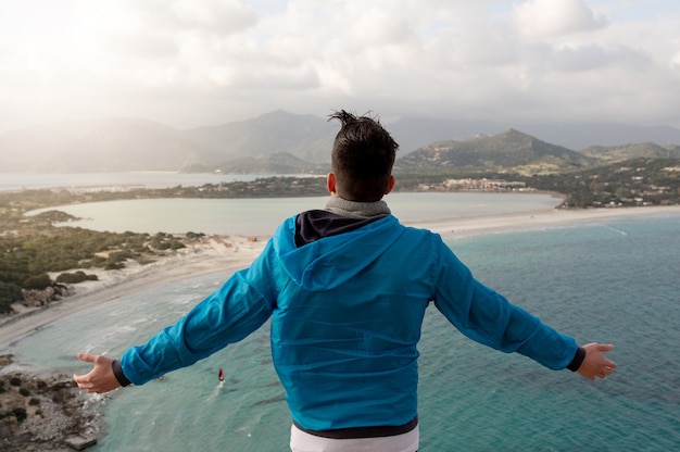 Vue arrière d'un homme méconnaissable debout sur une falaise à bras ouverts profiter de la brise marine et du vent