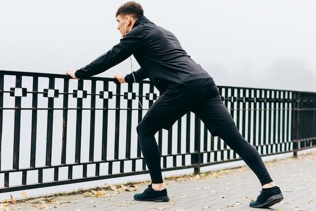 Vue arrière d'un homme musclé athlétique qui s'étend en plein air le matin sur le fond de la nature du brouillard Homme de remise en forme faisant de l'exercice dans le parc Concept de personnes et de sport