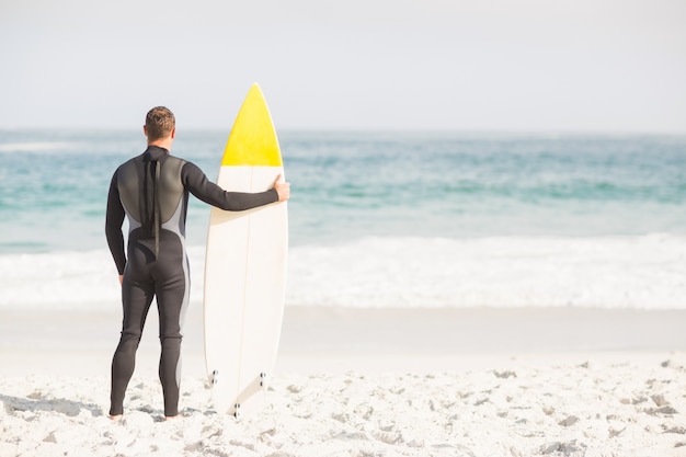 Photo vue arrière de l'homme avec la planche de surf debout sur la plage