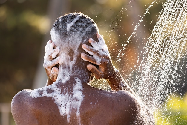 Vue arrière homme prenant une douche à l'extérieur