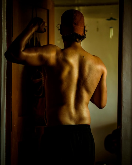 Vue arrière d'un homme sans chemise fléchissant ses muscles debout à la maison
