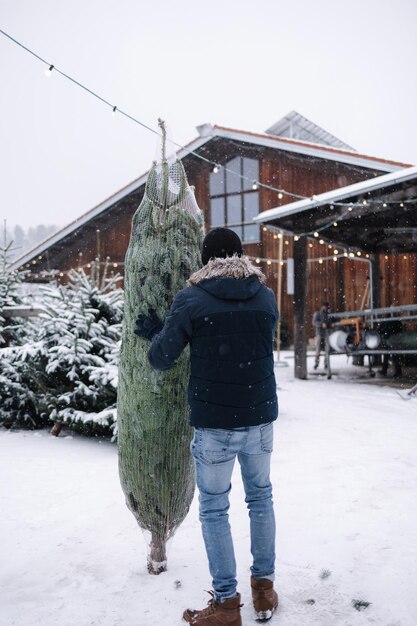 Vue arrière de l'homme se tient au centre de la foire de l'arbre de Noël et choisit le sapin