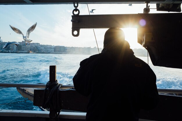 Photo vue arrière d'un homme en silhouette debout dans un bateau sur la mer contre le ciel