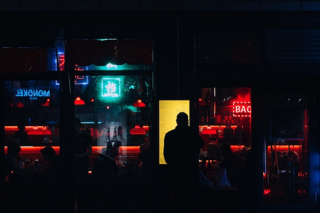 Vue arrière d'un homme en silhouette debout à l'extérieur d'un restaurant illuminé