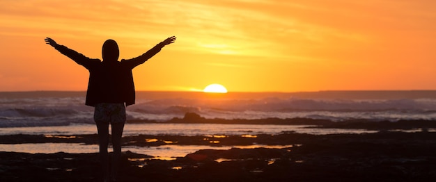 Photo vue arrière d'un homme en silhouette debout sur la plage au coucher du soleil