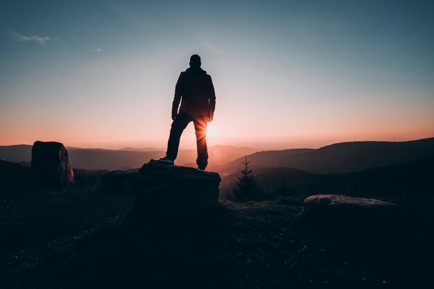 Vue arrière d'un homme en silhouette debout sur un rocher contre le ciel au coucher du soleil