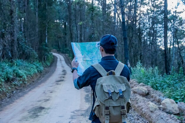 Vue arrière d'un homme tenant une carte alors qu'il se tient sur une route de terre contre le ciel