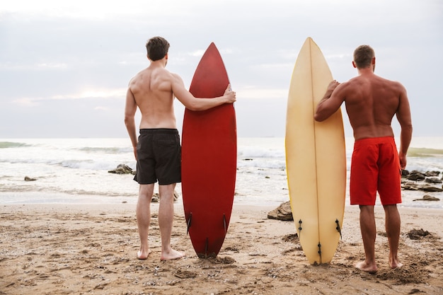 Vue arrière de l'image d'un jeune deux hommes amis surfeurs avec des surfs sur une plage à l'extérieur.