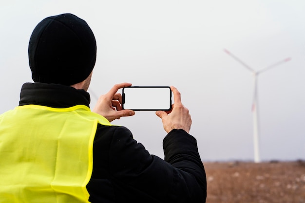 Photo vue arrière de l'ingénieur de sexe masculin à prendre des photos d'éoliennes sur le terrain