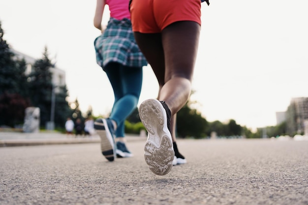 Vue arrière des jambes d'amis en vêtements de sport courant dans la ville Femmes multiethniques ayant un entraînement de fitness