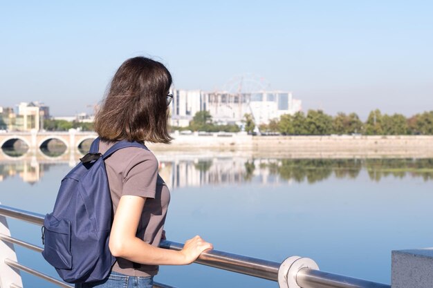 Une vue arrière d'un jeune étudiant aux cheveux bouclés un sac à dos bleu Debout dans un parc sur fond de rivière