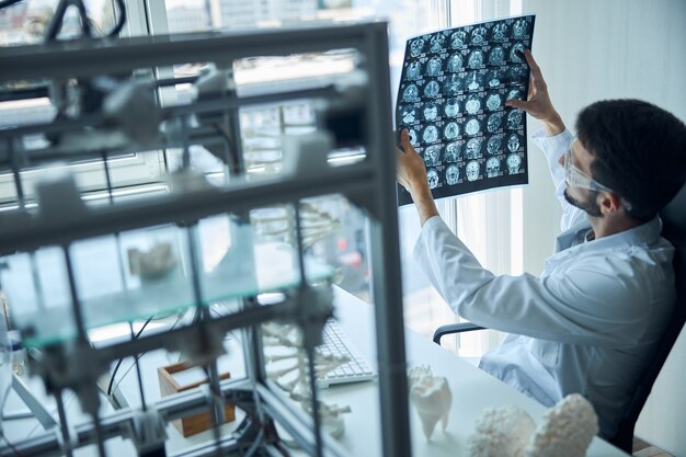 Vue arrière d'un jeune étudiant en médecine en blouse de laboratoire examinant l'IRM cérébrale