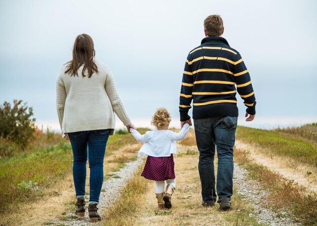 Photo vue arrière d'une jeune famille qui s'éloigne sur une route de campagne