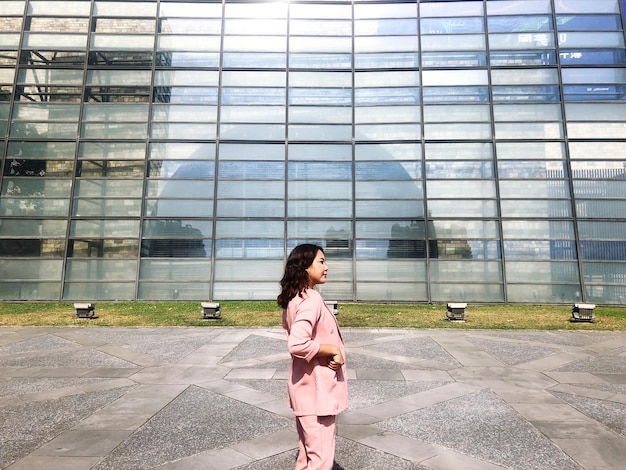 Vue arrière d'une jeune femme debout contre un bâtiment en verre