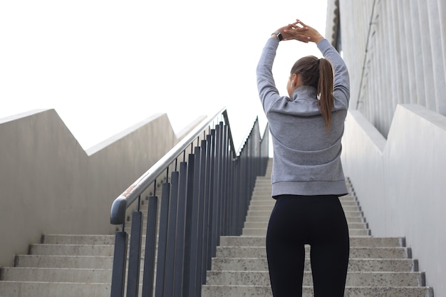 Vue arrière d'une jeune femme en forme et sportive faisant des étirements en plein air.