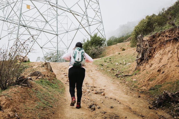 Vue arrière jeune femme latine de taille plus avec sac à dos, escalade une colline et randonnée dans un jour de brouillard