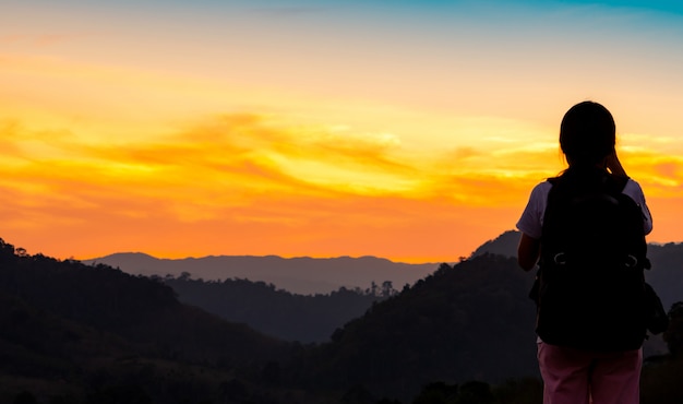 Vue arrière de la jeune femme regardant le magnifique coucher de soleil sur la couche de montagne