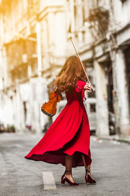 Vue arrière de la jeune femme en robe rouge tenant un violon