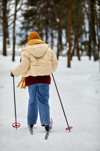 Vue arrière d'une jeune femme skiant dans la forêt d'hiver et profitant d'une activité à l'extérieur