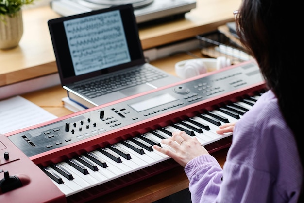 Vue arrière d'une jeune femme utilisant des partitions pour jouer du piano à table pendant la répétition à la maison