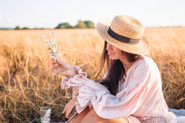 Vue arrière de la jeune fille dans le champ de blé. Belle femme en robe dans un chapeau de paille avec du blé mûr dans les mains