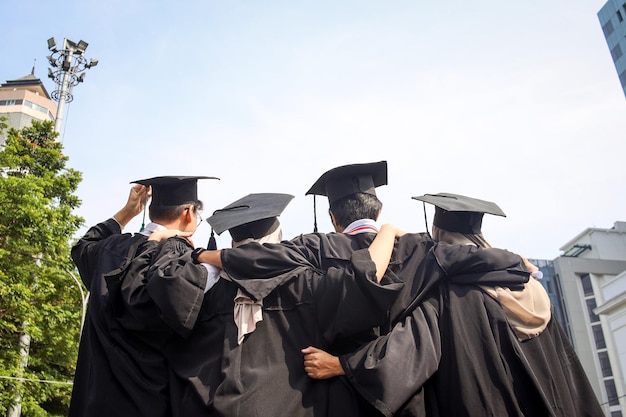 Vue arrière d'un jeune groupe d'amis diplômés multiraciaux heureux s'embrassant debout dans une rangée