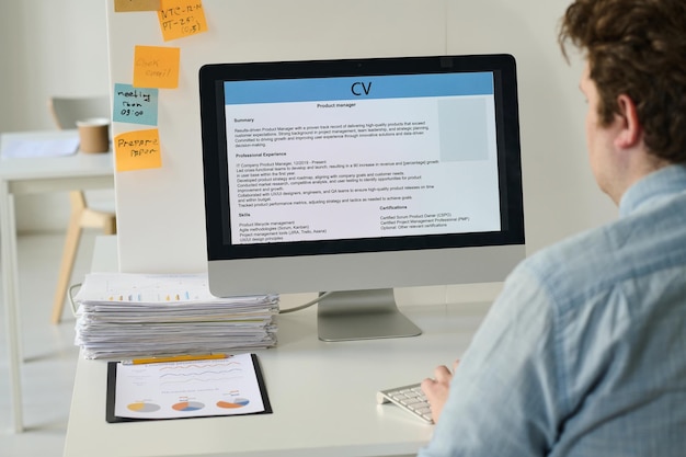 Vue arrière d'un jeune homme d'affaires assis sur son lieu de travail et utilisant un ordinateur pour publier son CV en ligne