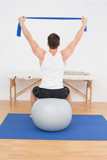 Vue arrière d&#39;un jeune homme assis sur une balle d&#39;yoga