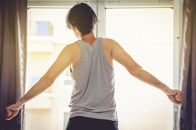 Photo vue arrière d'un jeune homme debout près de la fenêtre à la maison