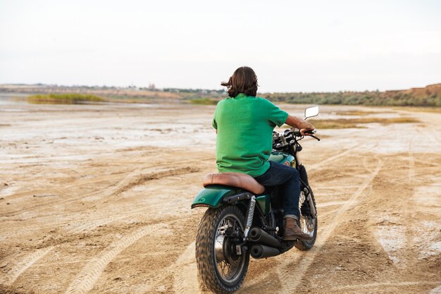 Vue arrière d'un jeune homme portant une tenue décontractée faisant de la moto à la plage