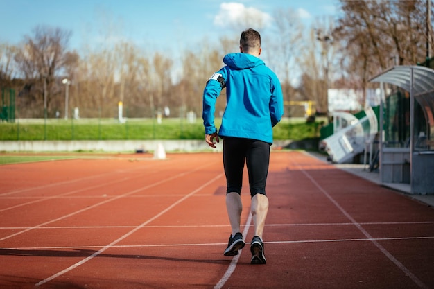 Vue arrière d'un jeune homme de sport en forme athlétique en pleine longueur du corps sur une piste en tartan sur le stade.