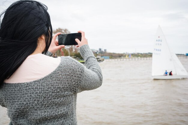 vue arrière d'une jeune touriste sur la jetée avec son téléphone prenant une photo des bateaux sur la rivière