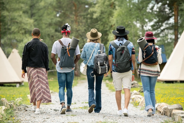 Vue arrière des jeunes avec des cartables marchant sur le camping du festival tout en trouvant tente