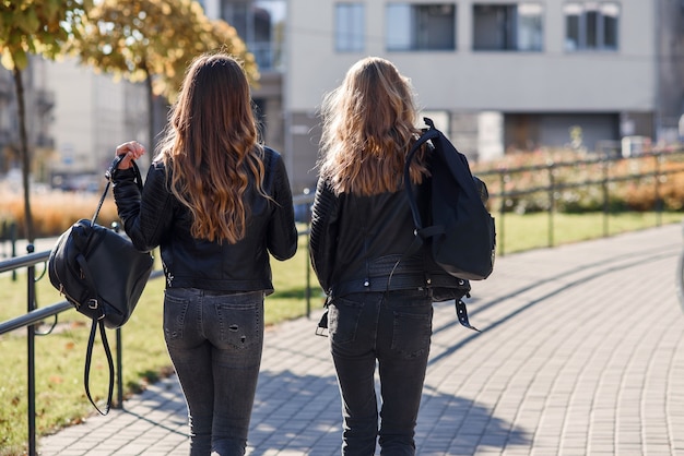 Vue arrière de jolies copines adolescentes avec des sacs à dos marchant dans la rue.