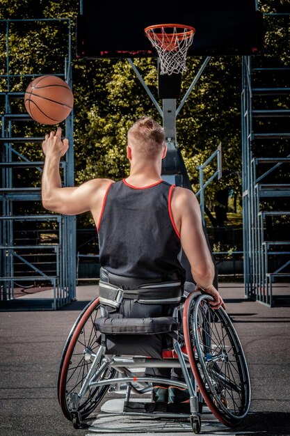 Vue arrière d'un joueur de basket-ball handicapé dans un fauteuil roulant faisant tourner le basket-ball sur son doigt sur un terrain de jeu ouvert.