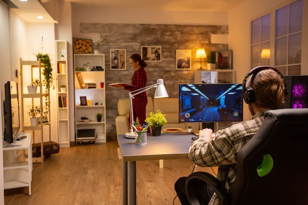 Photo vue arrière d'un joueur vidéo professionnel jouant sur un pc puissant tard dans la nuit dans le salon.