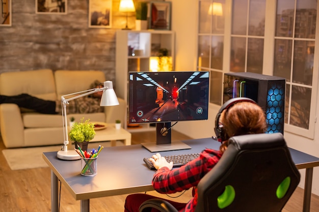 Vue arrière d'une joueuse jouant sur un ordinateur puissant tard dans la nuit dans le salon.