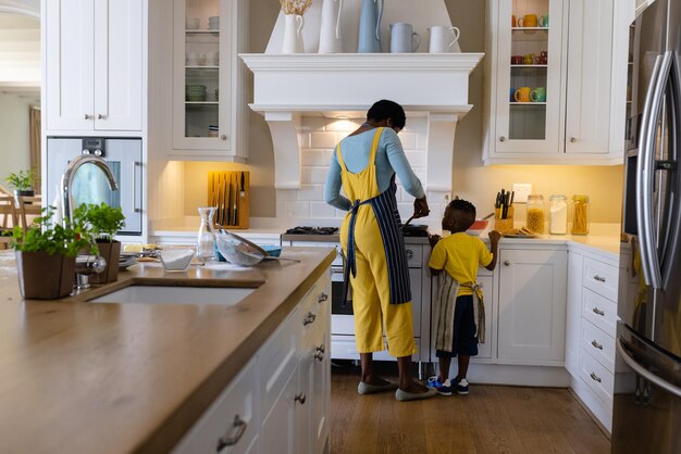 Photo vue arrière d'une mère afro-américaine avec son fils cuisinant des crêpes dans la cuisine. inaltéré, style de vie, famille, amour, convivialité, enfance, nourriture, préparation, apprentissage et concept de maison.