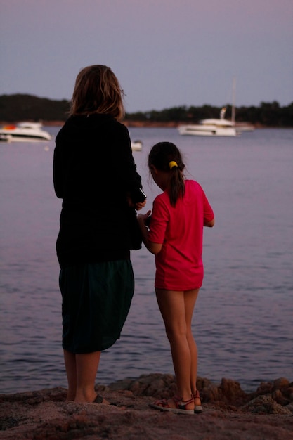 Photo vue arrière d'une mère et d'une fille debout sur le rivage sur la plage contre un ciel clair