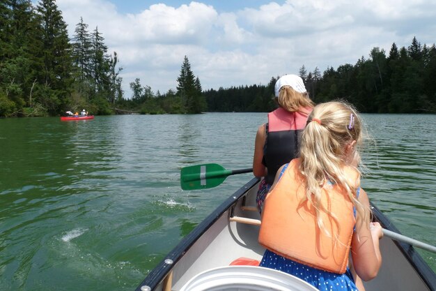 Vue arrière d'une mère avec sa fille en bateau à rames sur le lac contre un ciel nuageux