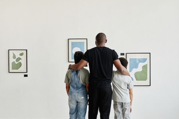 Photo vue arrière minimale à la famille afro-américaine regardant des peintures dans une galerie d'art moderne, espace de copie