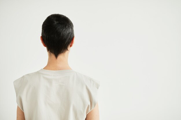 Vue arrière minimale portrait d'une femme confiante aux cheveux courts debout contre le blanc et célébrant la récupération, espace de copie