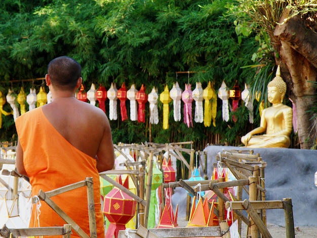 Photo vue arrière d'un moine debout devant des lanternes colorées à l'extérieur d'un temple bouddhiste