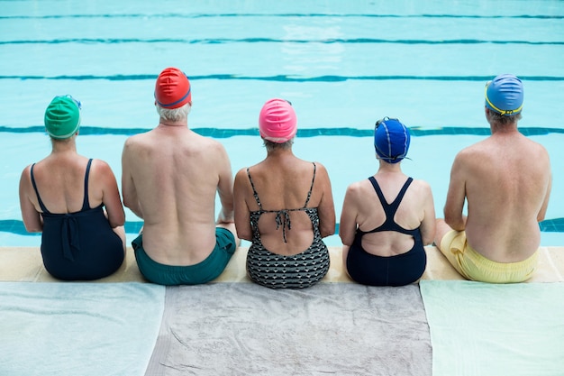 Vue arrière des nageurs seniors assis au bord de la piscine