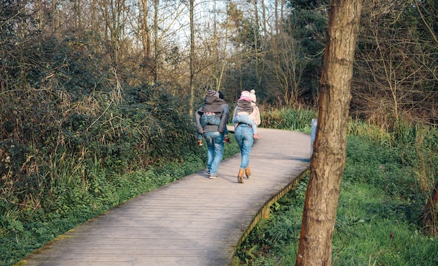 Vue arrière des parents donnant un tour de ferroutage aux enfants tout en courant sur un sentier en bois dans la forêt